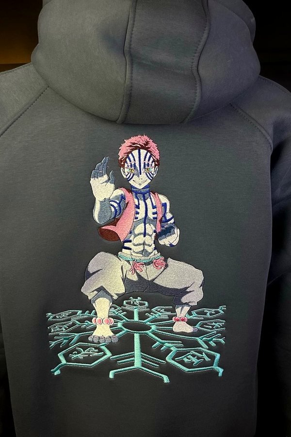 Olive-grey heavyweight hoodie, back view, embroidered with a standing figure above a pale geometric crest